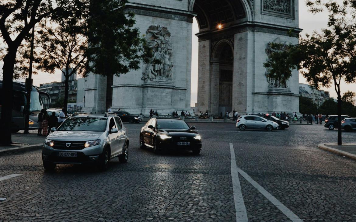 Image de plusieurs voitures (dont des SUV) passant devant l'arc de triomphe, Paris