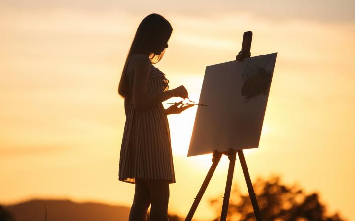 Femme qui peint devant un coucher de soleil