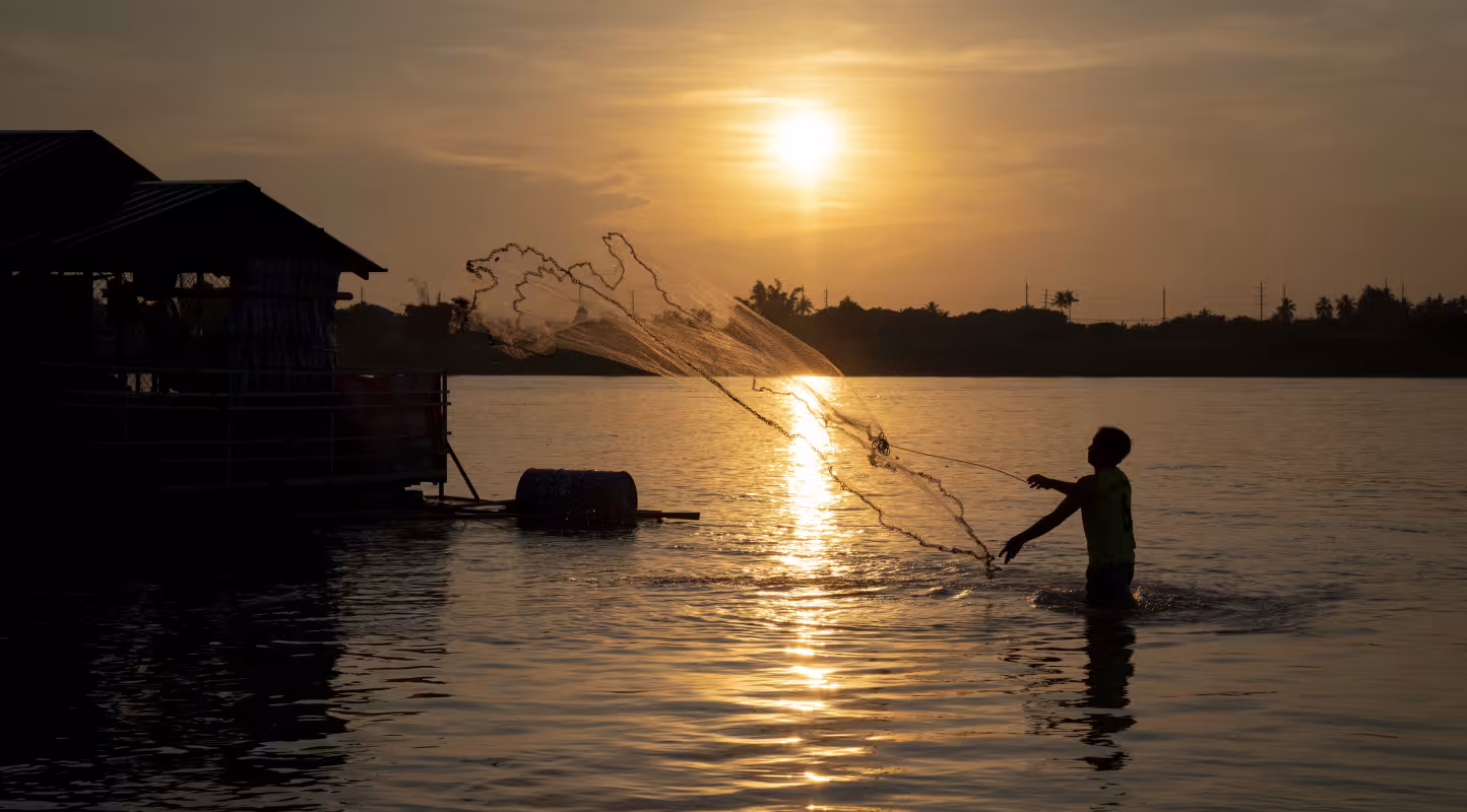 Un pêcheur lance son filet alors que le soleil se couche sur le fleuve Mékong, à Vientiane, RDP Lao.
