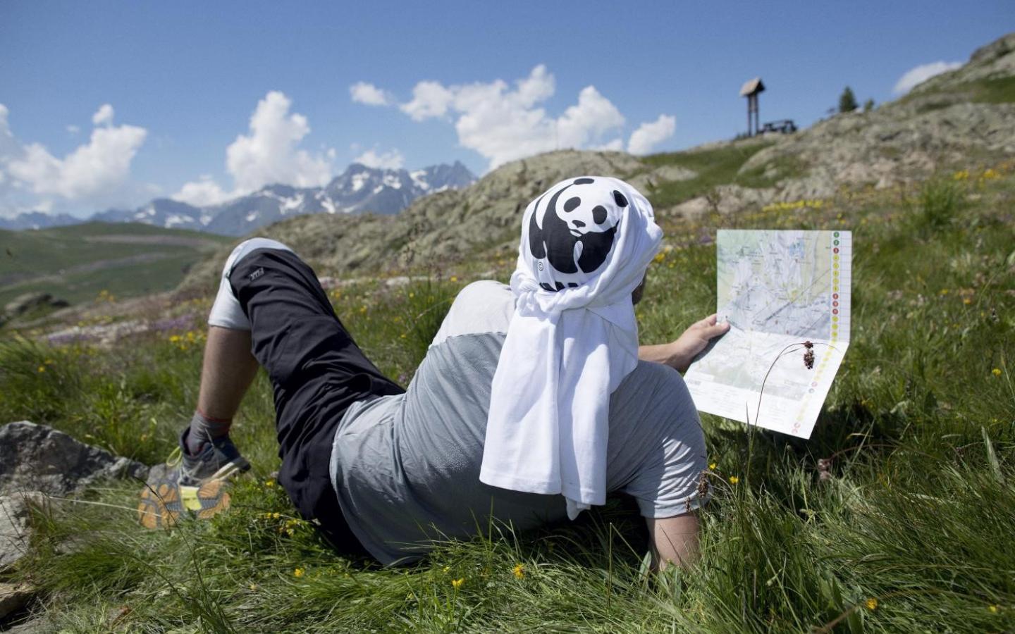 Un pandathlète se repose dans l'herbe en lisant la carte d'orientation du parcours à l'Alpe d'Huez (France)