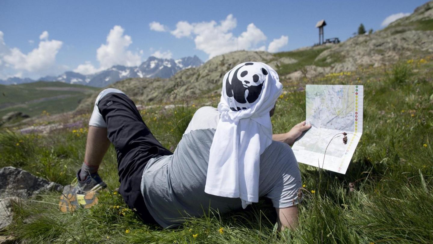Un pandathlète se repose dans l'herbe en lisant la carte d'orientation du parcours à l'Alpe d'Huez (France)