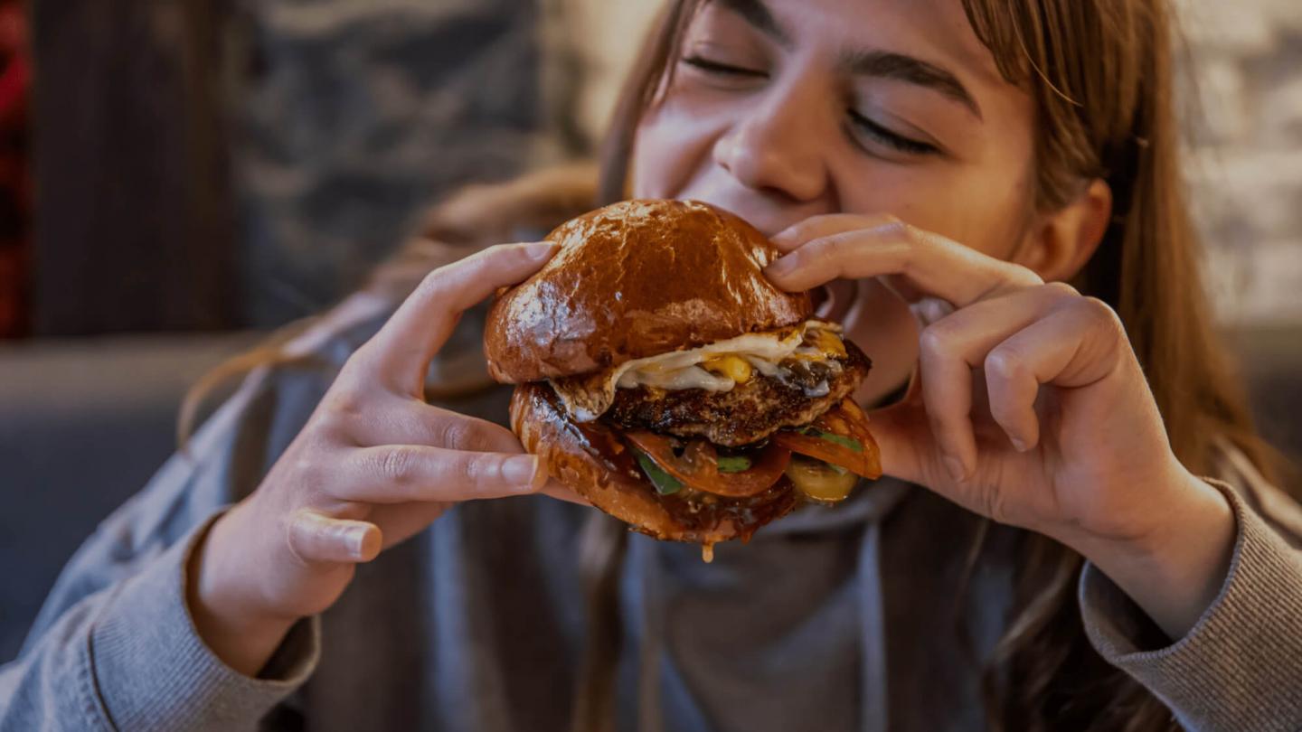 Jeune fille mangeant un hamburger appétissant, défi au mythe des protéines animales