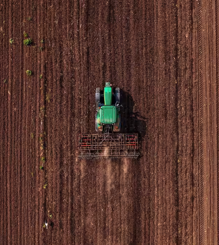 Tracteur vert équipé d'une fraise effectuant le labour avant les semailles, vue aérienne par drone